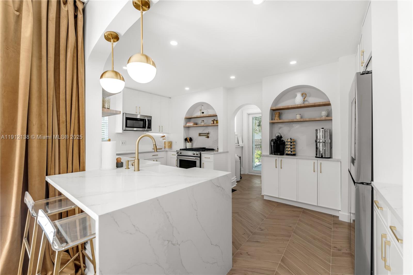 A modern kitchen features white cabinetry, marble countertops, gold fixtures, and arched wall niches — 1601 Washington St, Hollywood FL 33020, HOLLYWOOD, FL