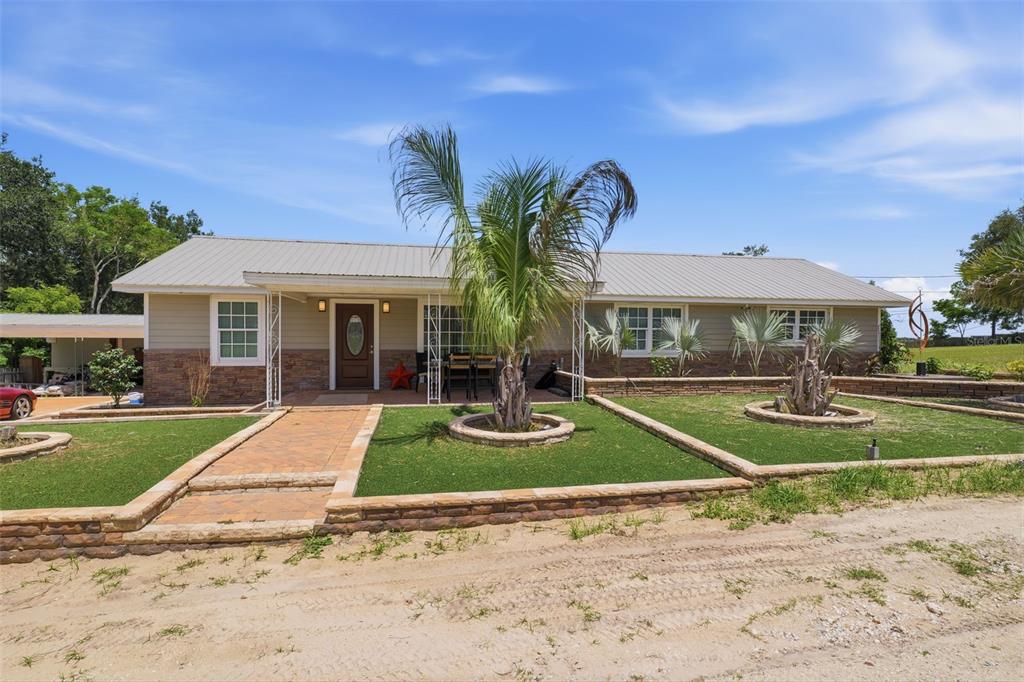 A single-story house with a metal roof, stone facade, and tiered landscaping in the front — 8744 GALL BLVD, ZEPHYRHILLS, FL