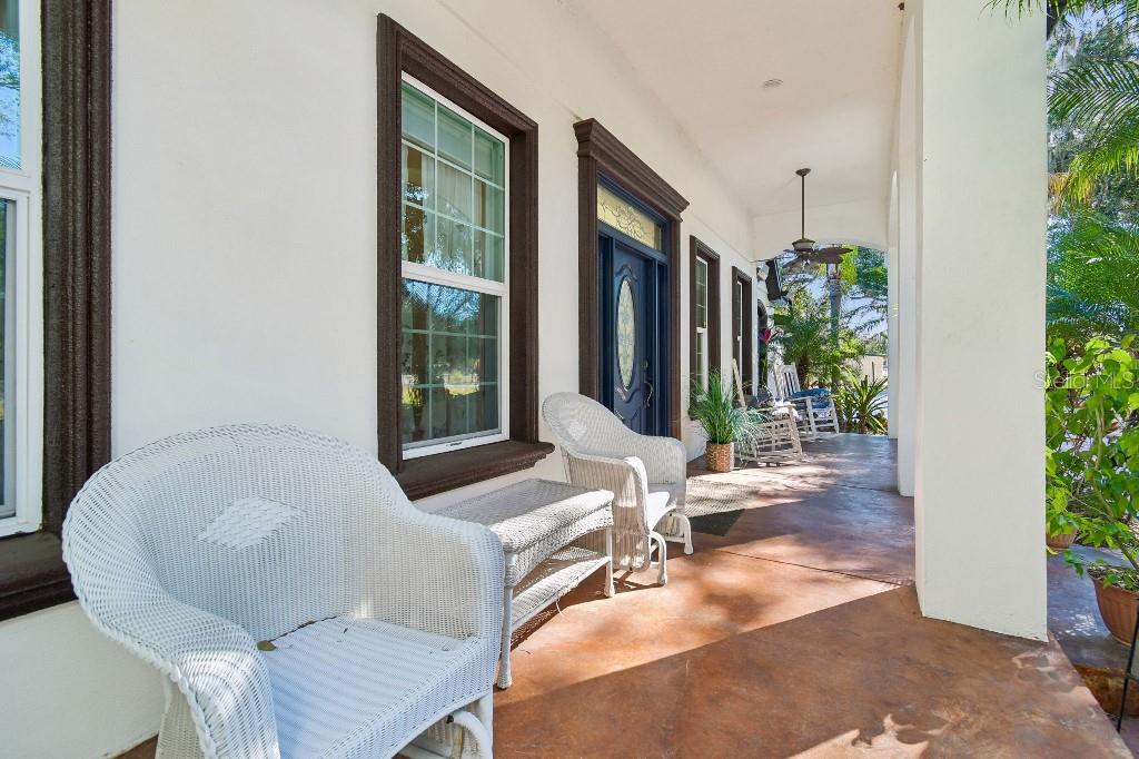 A covered porch features white wicker furniture, a blue front door, and stained concrete flooring — 3302 JAP TUCKER ROAD, PLANT CITY, FL