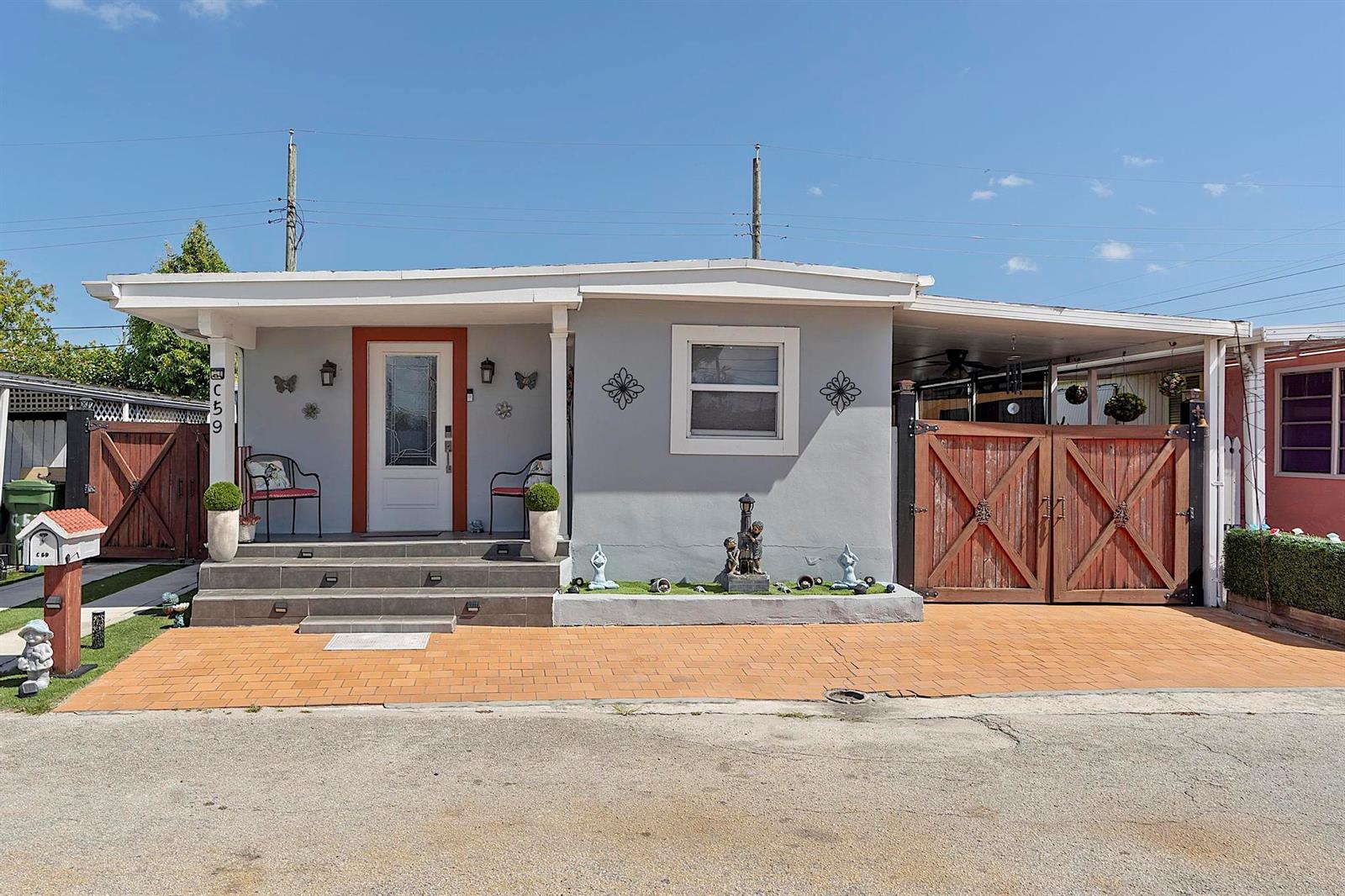 A single-story gray house features a front porch, a carport with wooden gates, and pavers — 3205 W 16th Avenue, Hialeah FL 33012, HIALEAH, FL
