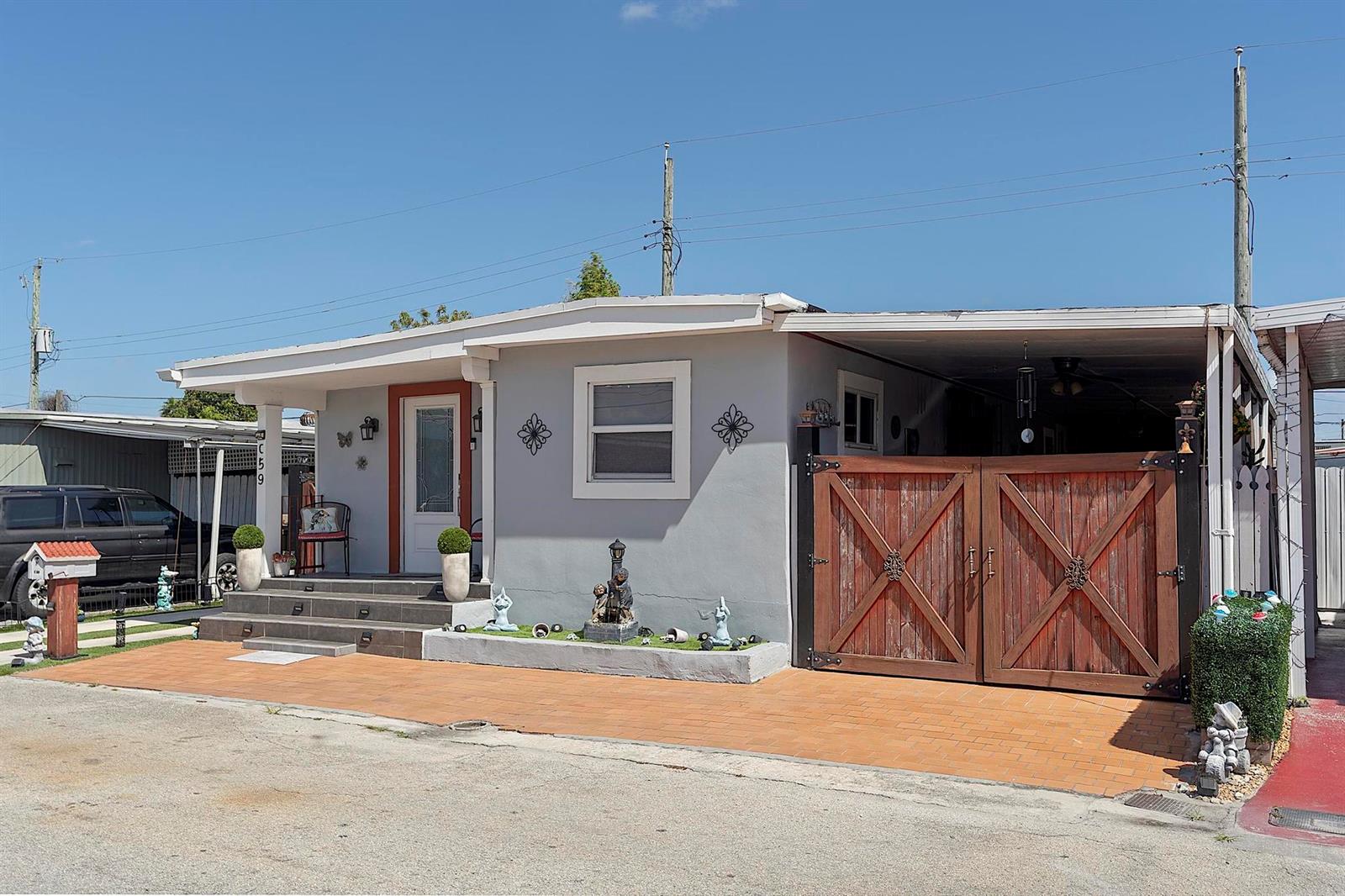 A light gray single-story house features a front porch, a carport with wooden gates, and pavers — 3205 W 16th Avenue, Hialeah FL 33012, HIALEAH, FL