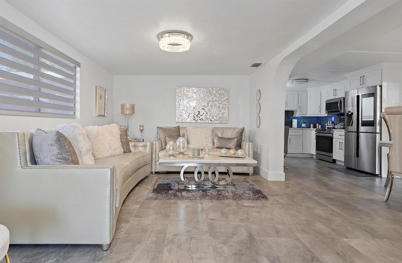 A living room with white sofas and a coffee table opens into a modern kitchen — 3205 W 16th Avenue, Hialeah FL 33012, HIALEAH, FL