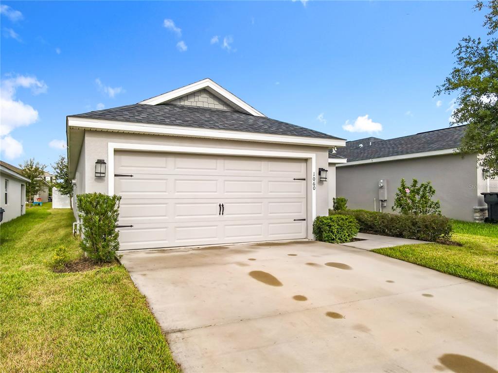 The exterior of a single-story house features a two-car garage and a concrete driveway — 1060 CASCADE DRIVE, DAVENPORT, FL