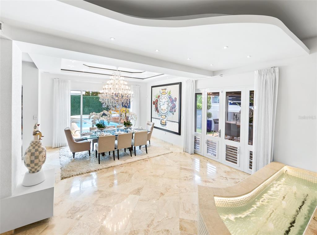 A dining room with a crystal chandelier, marble floors, and a view of a pool — Calle Boulevard URB. LOS ÁRBOLES DE MONTEHIEDRA, SAN JUAN, PR