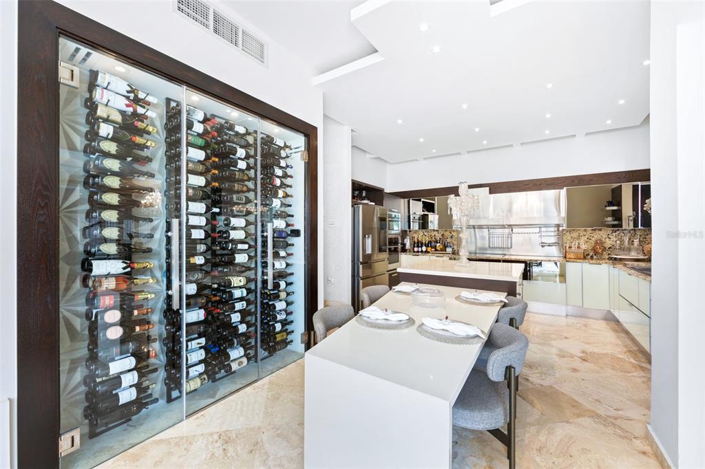 A modern kitchen features a glass-enclosed wine cellar, a white dining table, and marble flooring — Calle Boulevard URB. LOS ÁRBOLES DE MONTEHIEDRA, SAN JUAN, PR