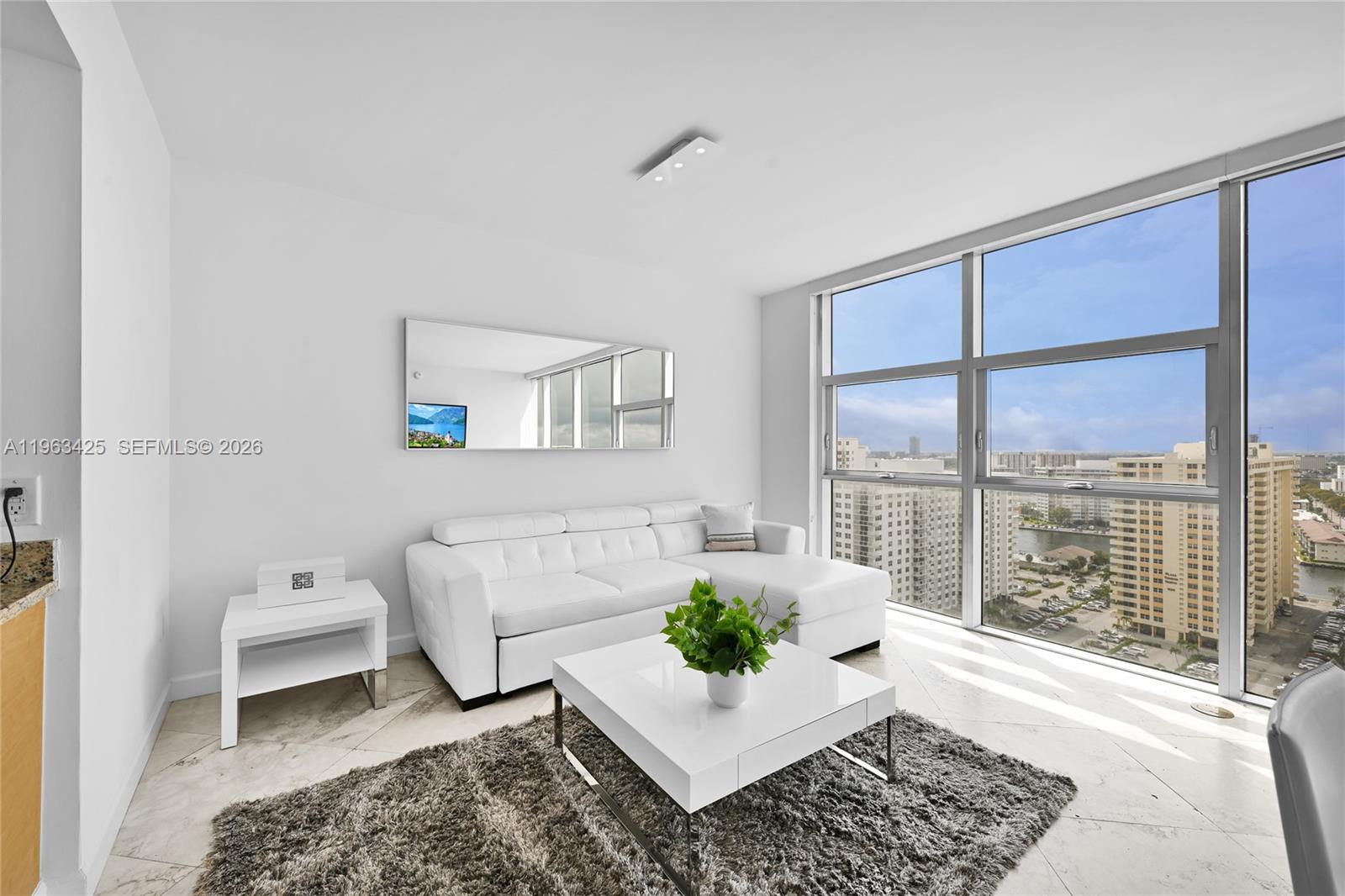 A modern living room features a white sectional sofa, coffee table, and floor-to-ceiling windows — 1830 S Ocean Dr # 1907, Hallandale Beach FL 33009, HALLANDALE BEACH, FL