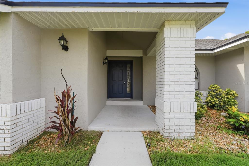 The front entrance of a house features a dark blue door, white brick columns, and landscaping — 1539 ELF STONE DRIVE, CASSELBERRY, FL