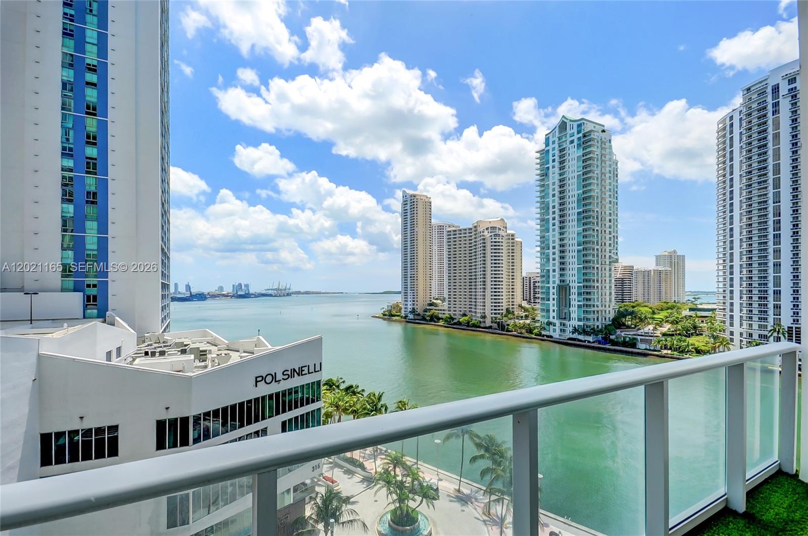 A balcony view overlooks a bay, nearby high-rise buildings, and a commercial office building — 300 S Biscayne Bluv # 1022, Miami FL 33131, MIAMI, FL