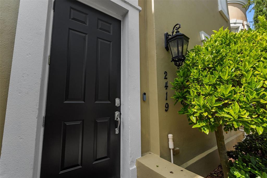 A black front door with white trim sits next to a house number and shrubbery — 2419 VICTORIA GARDENS LANE, TAMPA, FL