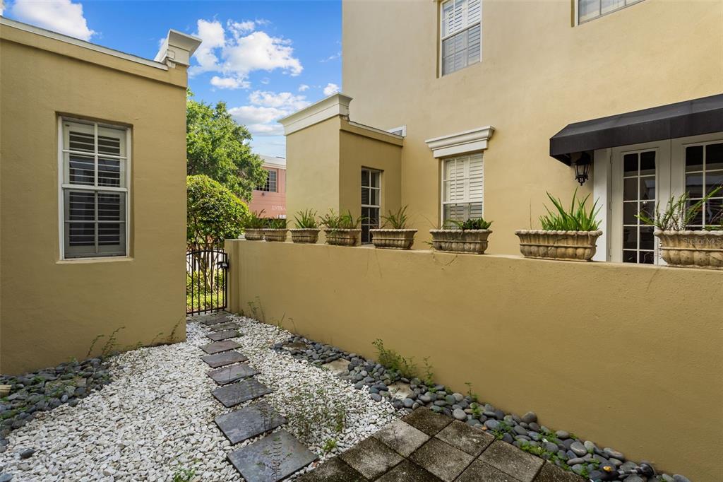 A stone-paved path leads through a small courtyard with potted plants along a stucco wall — 2419 VICTORIA GARDENS LANE, TAMPA, FL