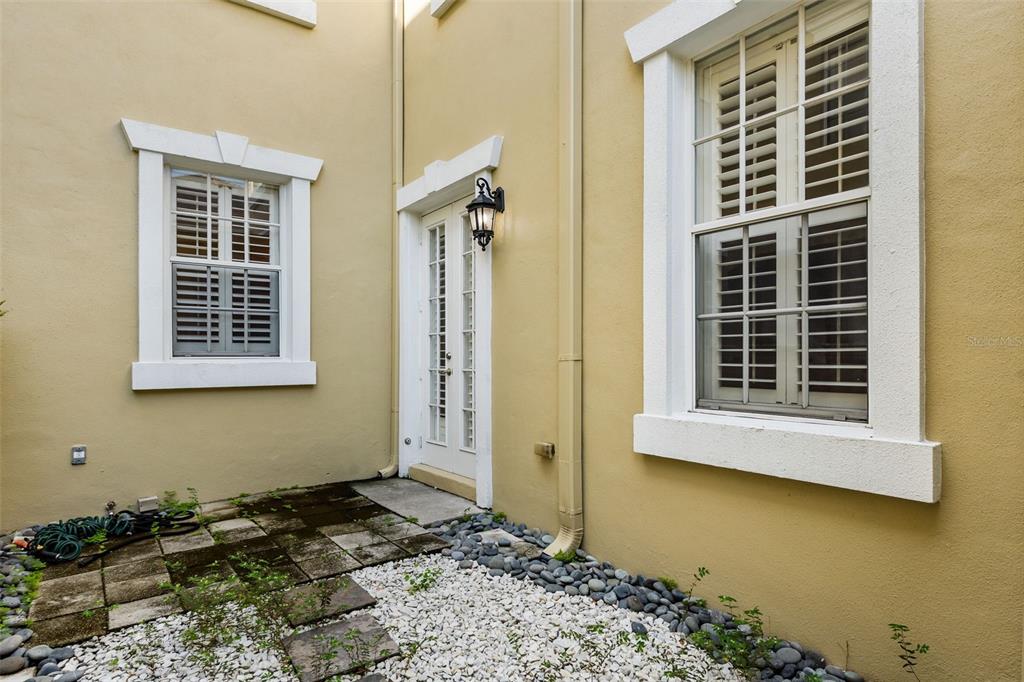 An exterior view of a tan building with two windows, a glass door, and landscaping — 2419 VICTORIA GARDENS LANE, TAMPA, FL