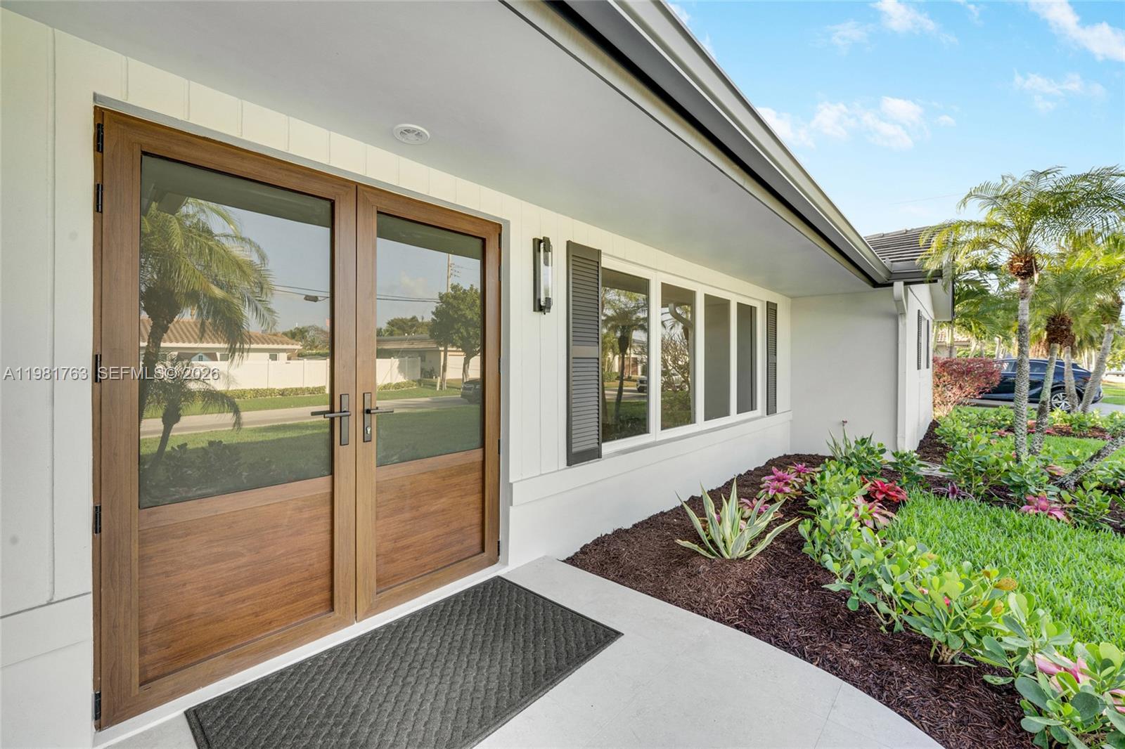 A modern home exterior features double wood-framed glass doors and a landscaped front garden — 4460 NE 25th Ave, Lighthouse Point FL 33064, LIGHTHOUSE POINT, FL