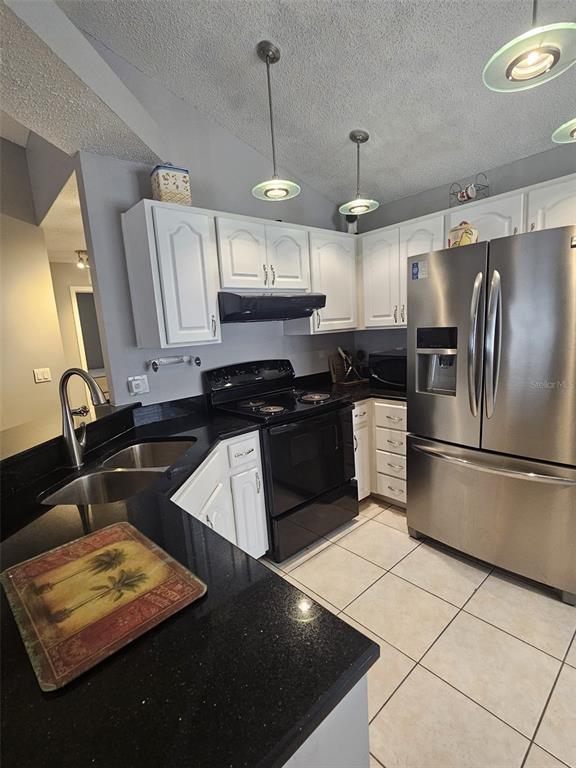 A kitchen features white cabinets, black countertops, stainless steel appliances, and tile flooring — 12718 TROWBRIDGE LANE, TAMPA, FL