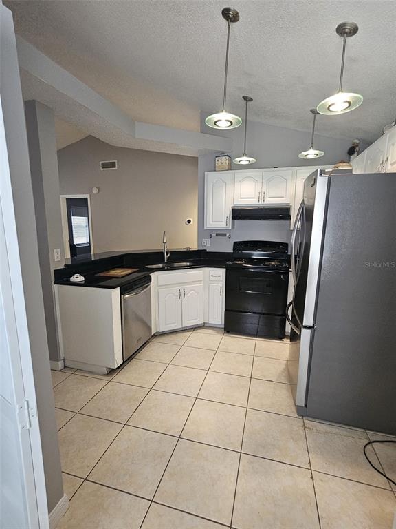 A kitchen features white cabinets, black countertops, stainless steel appliances, and light-colored floor tiles — 12718 TROWBRIDGE LANE, TAMPA, FL
