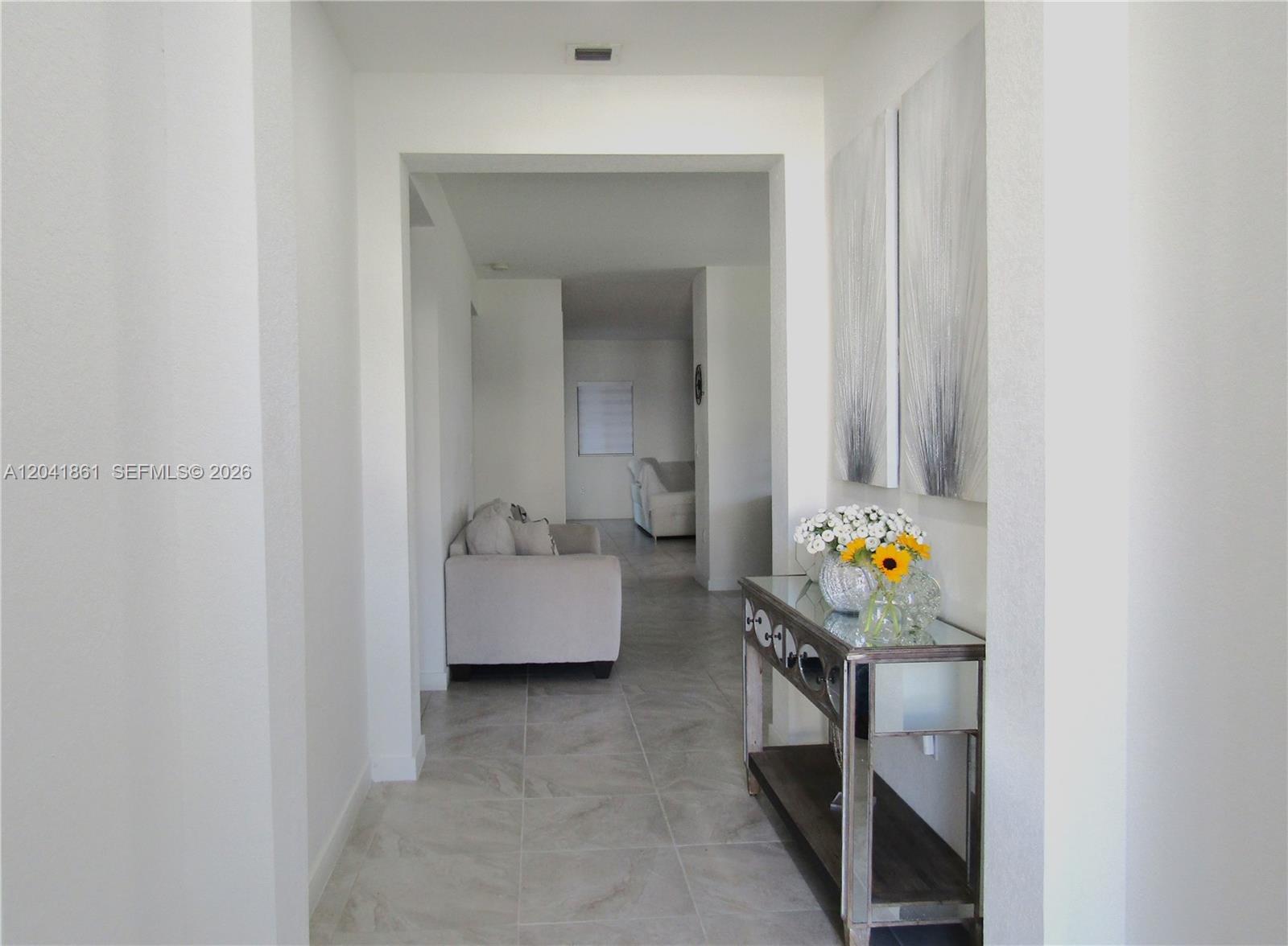 A tiled hallway leads to a living area with a mirrored console table and artwork — 16825 SW 109th Pl, Miami FL 33157, MIAMI, FL