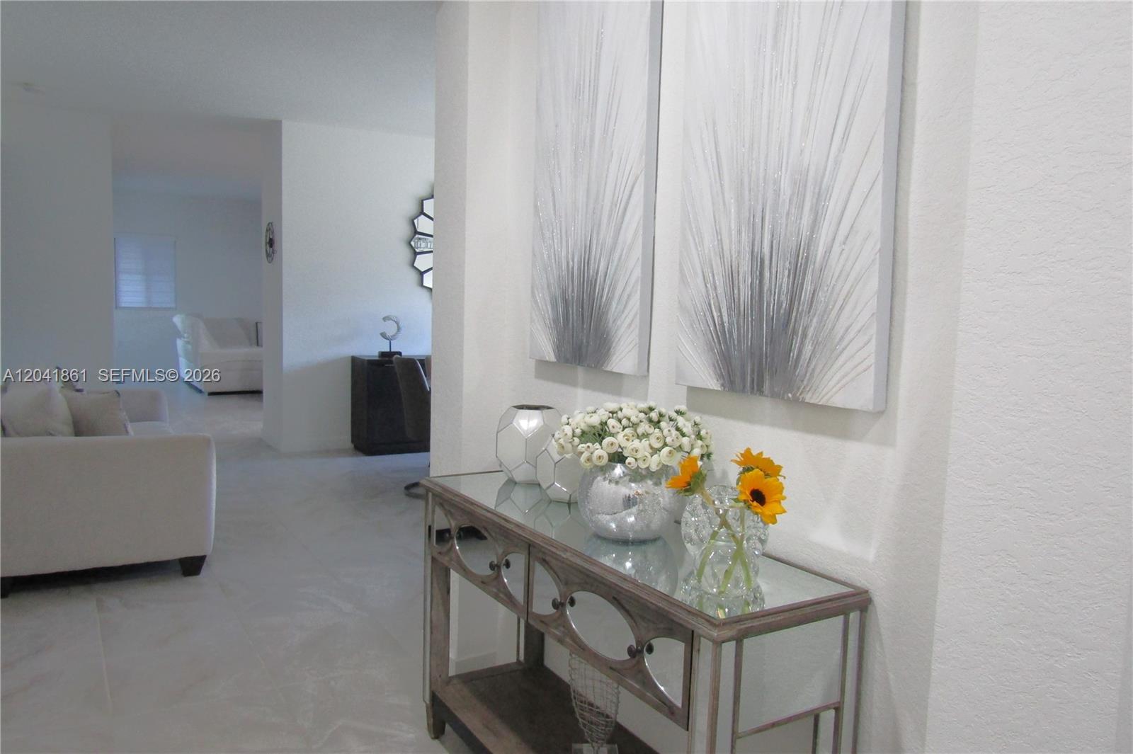 A mirrored console table with floral arrangements sits in a hallway beneath two abstract paintings — 16825 SW 109th Pl, Miami FL 33157, MIAMI, FL
