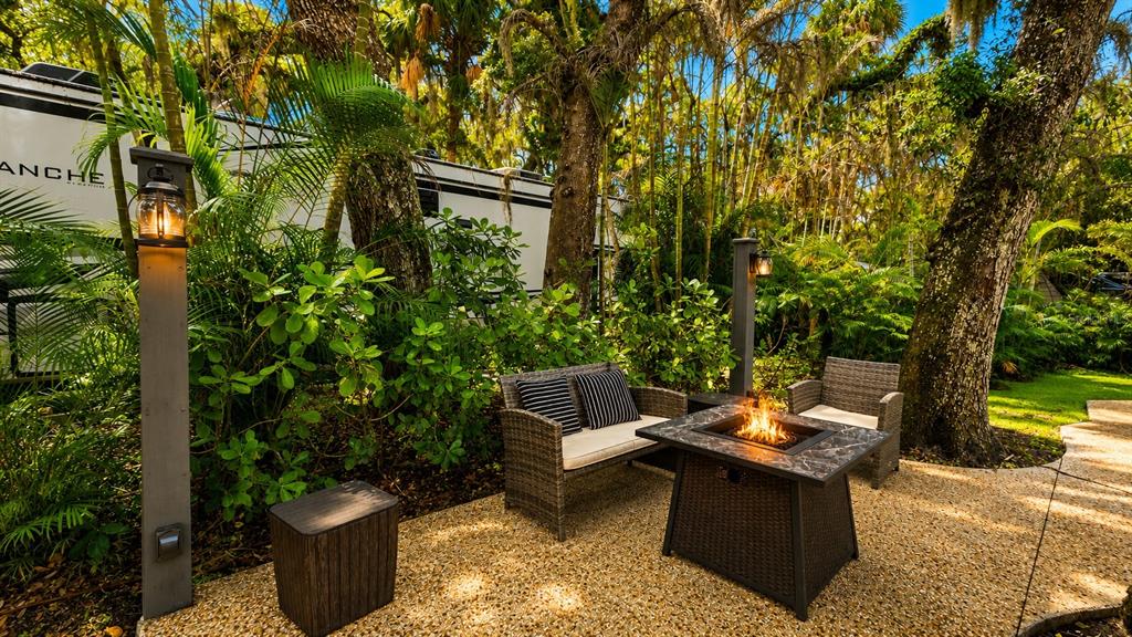 A patio features a fire pit, wicker seating, and outdoor lighting in a wooded setting — 312 GATOR ALLEY, LAKE WALES, FL