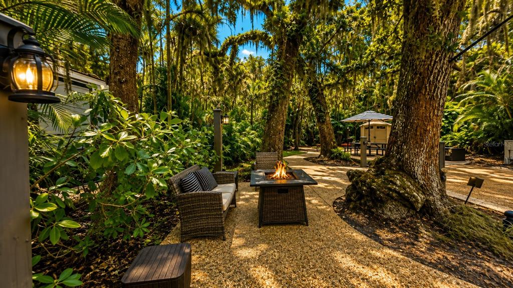 A patio with a fire pit, wicker furniture, and large trees in a wooded setting — 312 GATOR ALLEY, LAKE WALES, FL