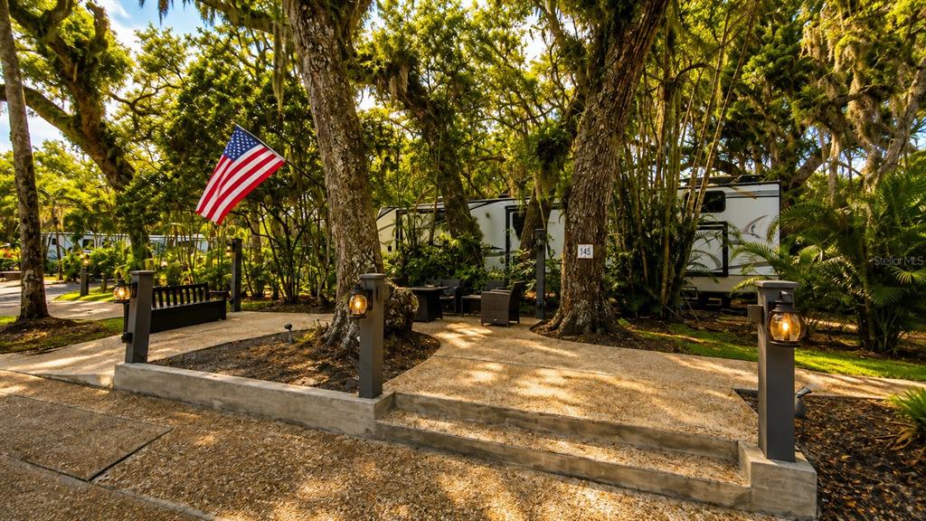 An outdoor patio area with a gravel surface, seating, and an American flag near trees — 312 GATOR ALLEY, LAKE WALES, FL