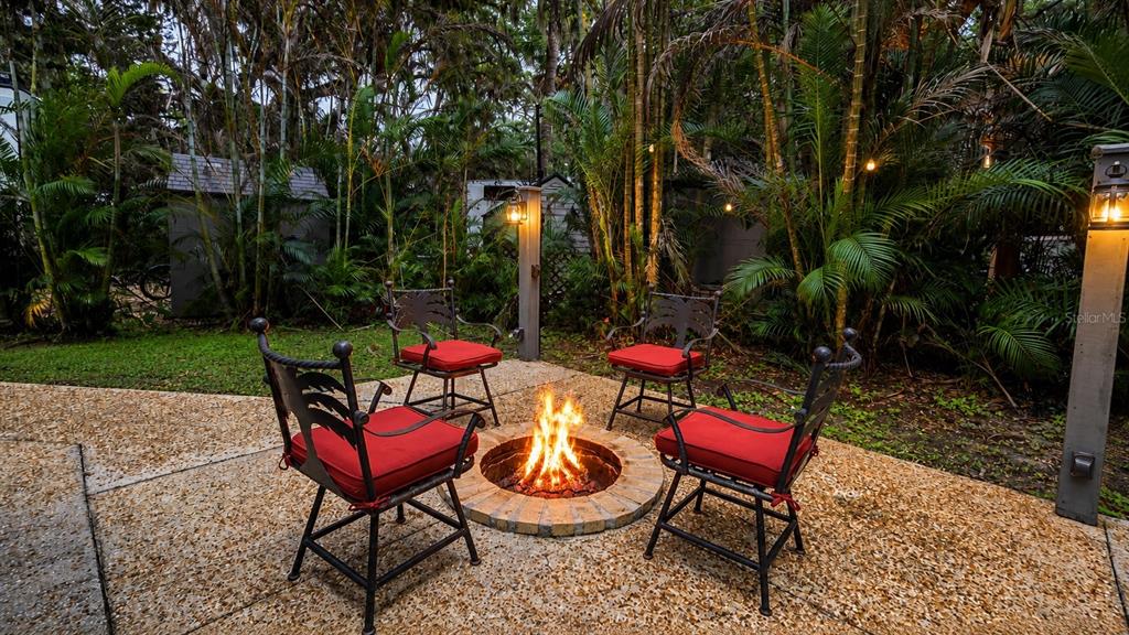 A backyard patio features a circular stone fire pit surrounded by four chairs with red cushions — 312 GATOR ALLEY, LAKE WALES, FL