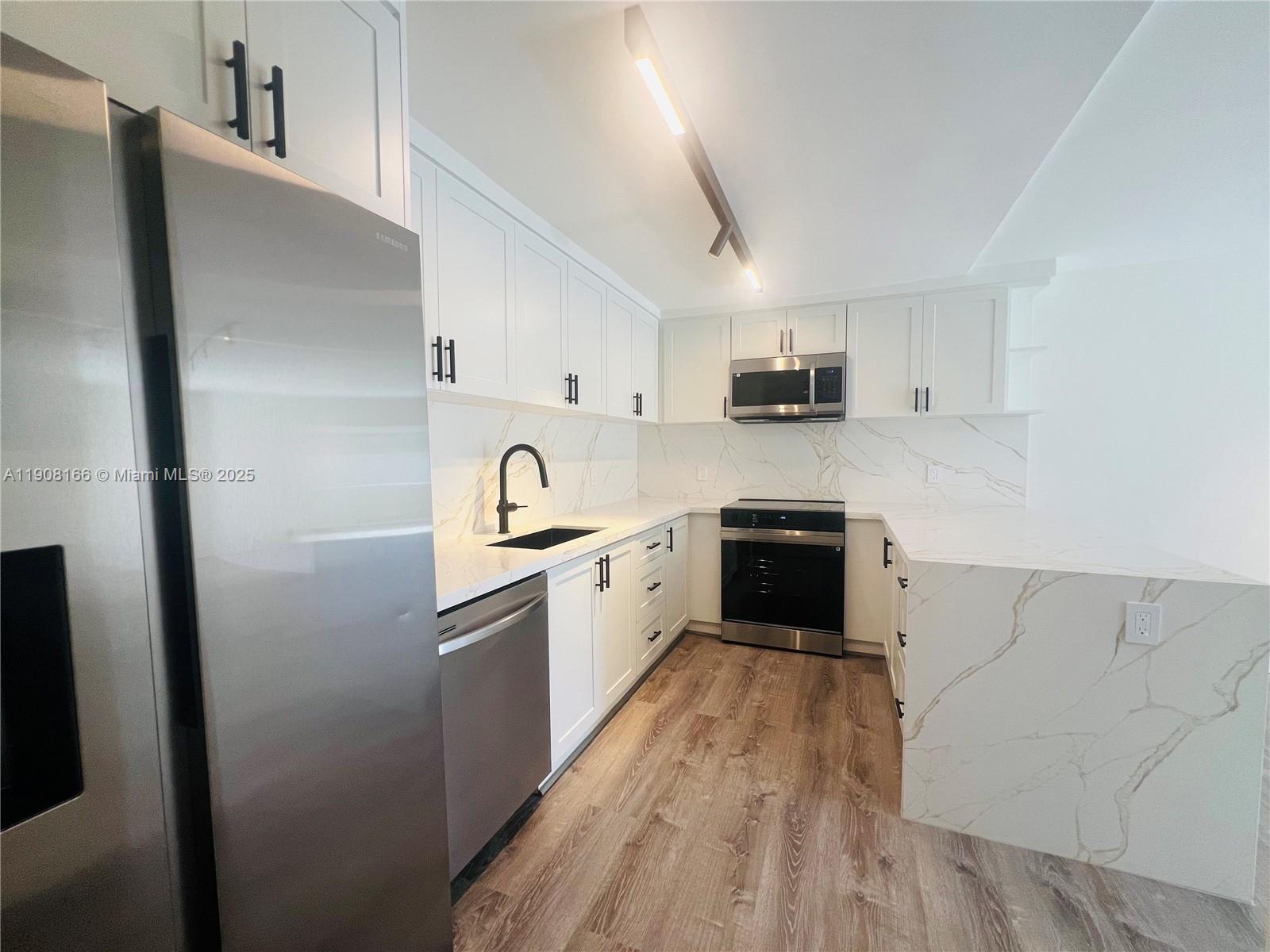 A modern kitchen features white cabinets, stainless steel appliances, and marble-patterned countertops and backsplash — 201 Jefferson Ave # 4C, Miami Beach FL 33139, MIAMI BEACH, FL