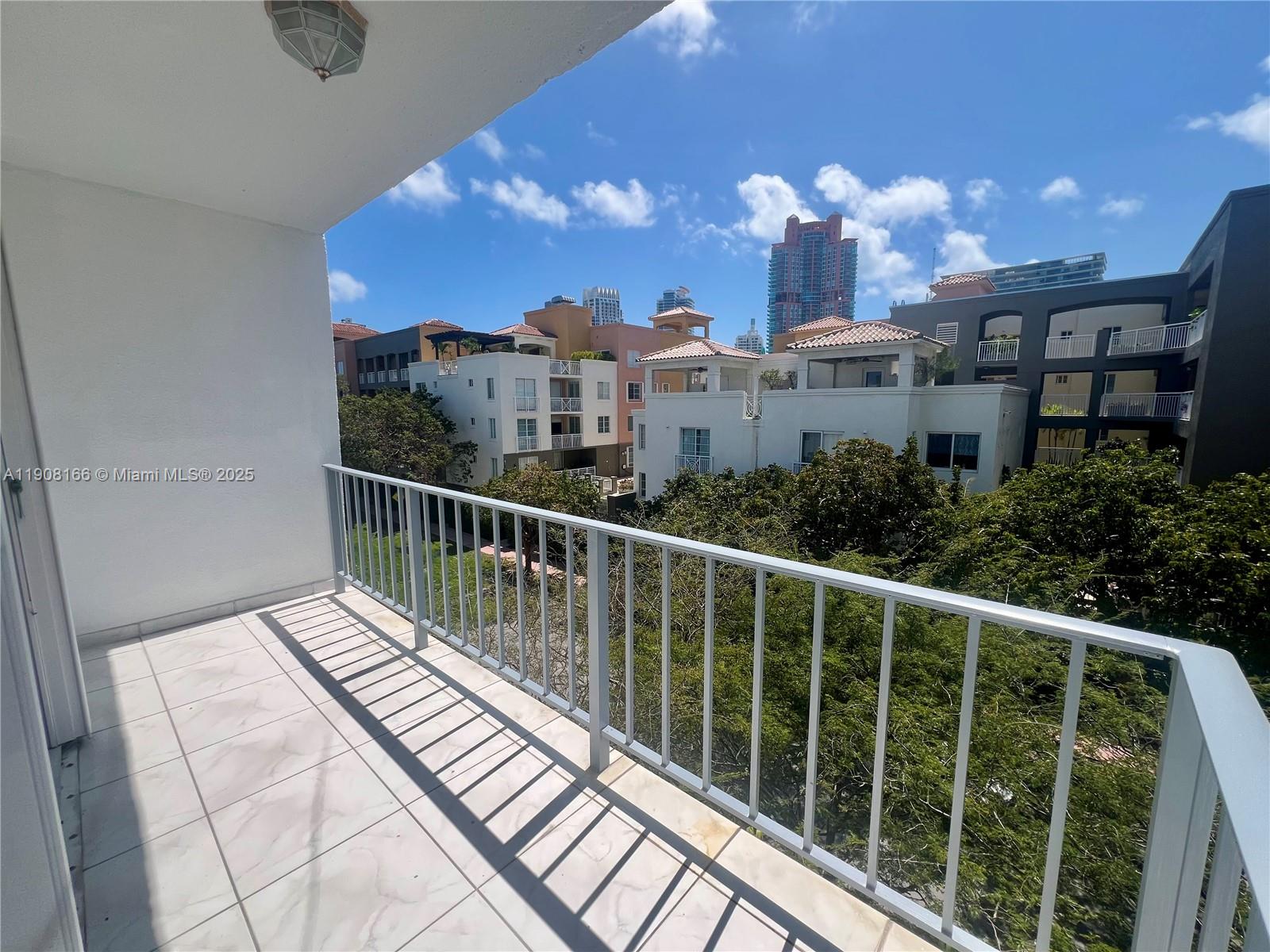 A balcony with white tiled flooring and a metal railing overlooks trees and buildings — 201 Jefferson Ave # 4C, Miami Beach FL 33139, MIAMI BEACH, FL