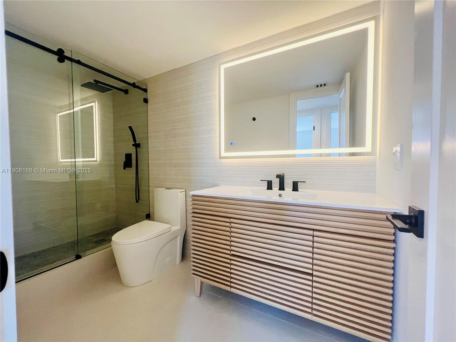 A modern bathroom features a slatted wood vanity, a backlit mirror, and a glass shower — 201 Jefferson Ave # 4C, Miami Beach FL 33139, MIAMI BEACH, FL