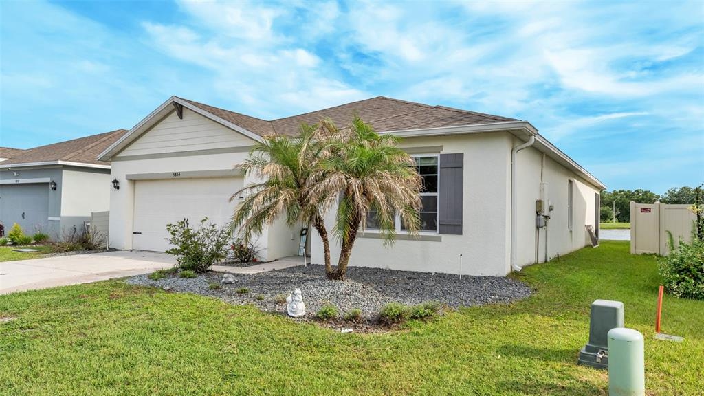 A single-story house with a beige stucco exterior, a two-car garage, and a palm tree — 5853 ARLINGTON RIVER DRIVE, LAKELAND, FL