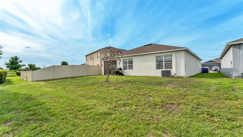 The backyard of a single-story house features a vinyl fence, lawn, and air conditioning unit — 5853 ARLINGTON RIVER DRIVE, LAKELAND, FL
