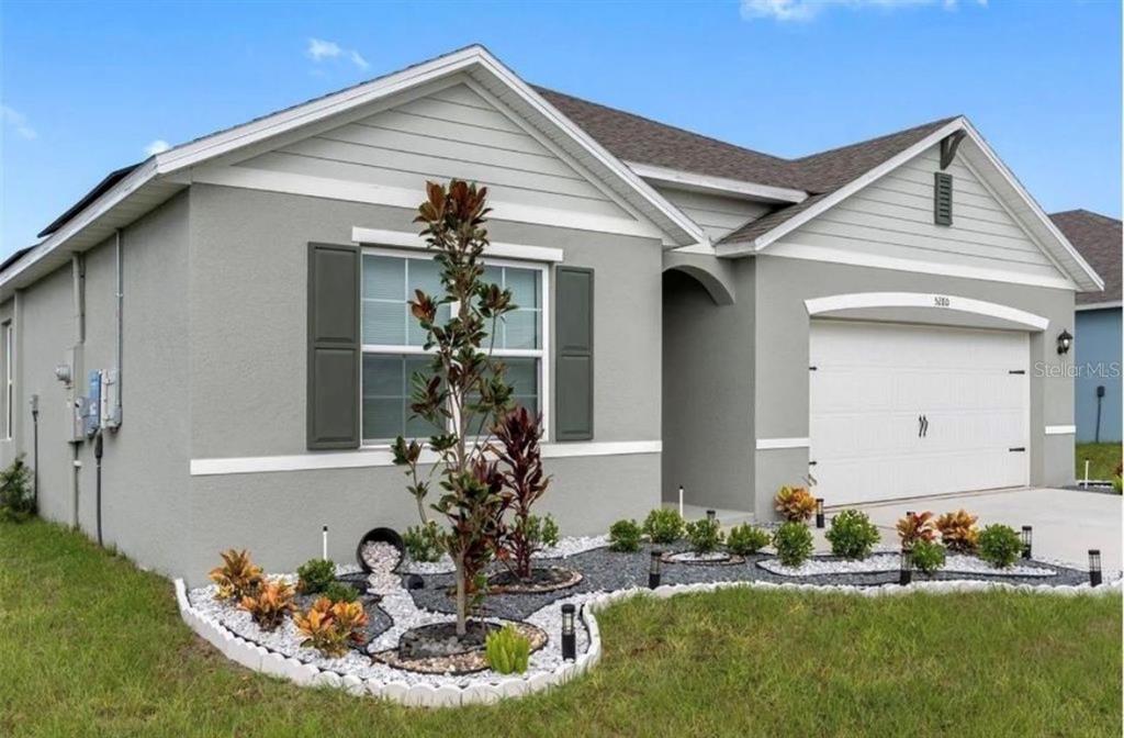 A single-story house with gray stucco siding, a two-car garage, and landscaped front yard — 5280 MADDIE DRIVE, HAINES CITY, FL