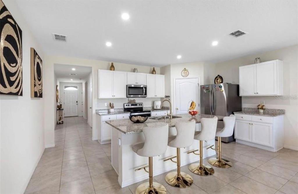 A kitchen features white cabinets, granite countertops, a central island with bar seating, and tile flooring — 5280 MADDIE DRIVE, HAINES CITY, FL