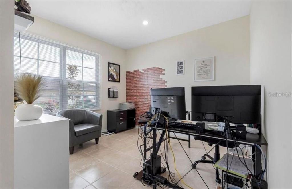 A home office features a desk with two monitors, a gray armchair, and brick-patterned wallpaper — 5280 MADDIE DRIVE, HAINES CITY, FL