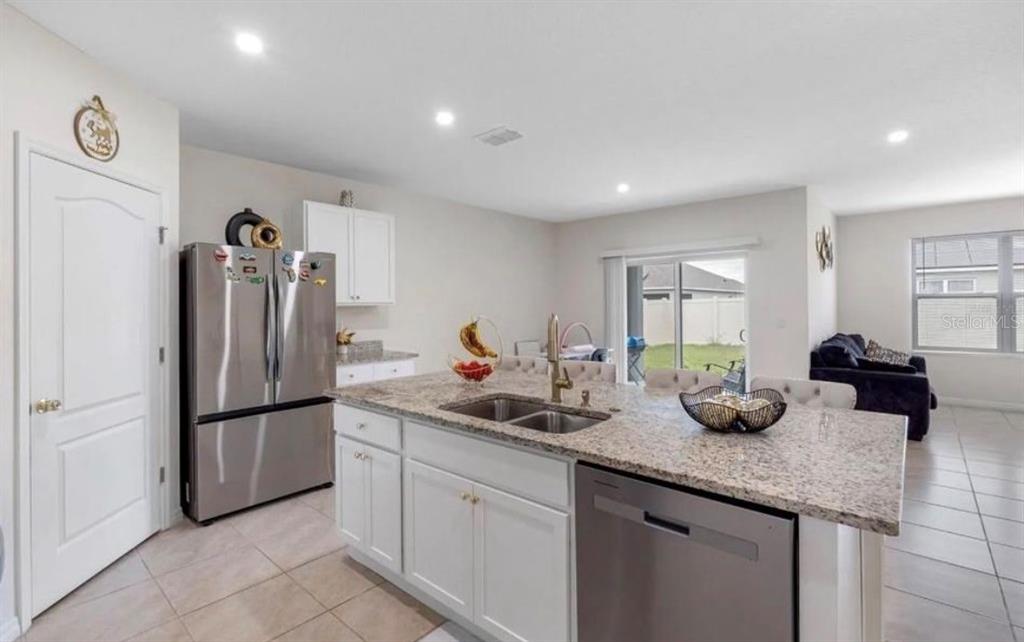 A kitchen features a granite-topped island, stainless steel appliances, white cabinetry, and tile flooring — 5280 MADDIE DRIVE, HAINES CITY, FL
