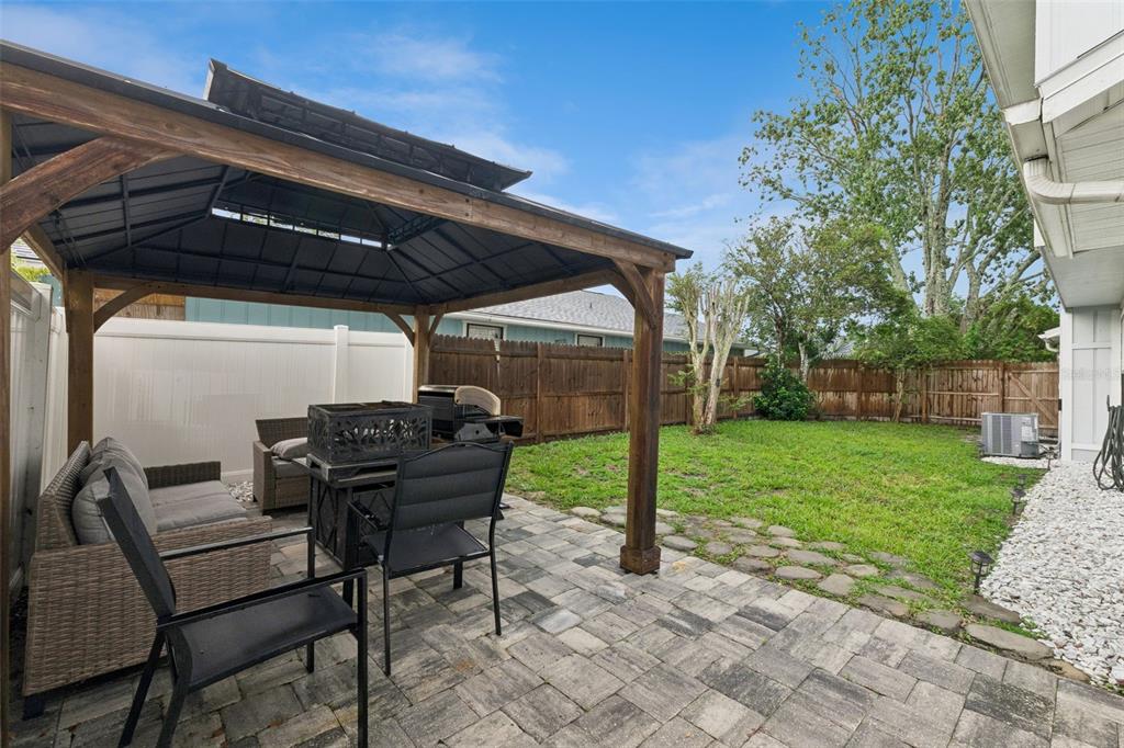 A backyard features a wooden gazebo over a paver patio with outdoor furniture and grass — 1197 SOUTHFORK COURT, PORT ORANGE, FL