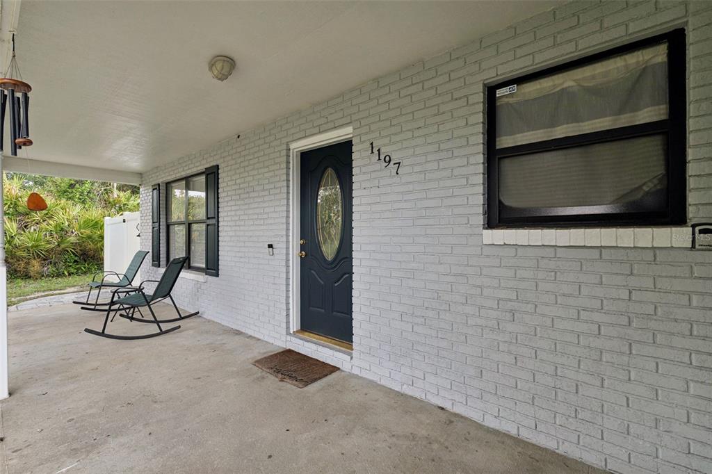 A covered porch features a gray brick exterior, a dark front door, and two rocking chairs — 1197 SOUTHFORK COURT, PORT ORANGE, FL