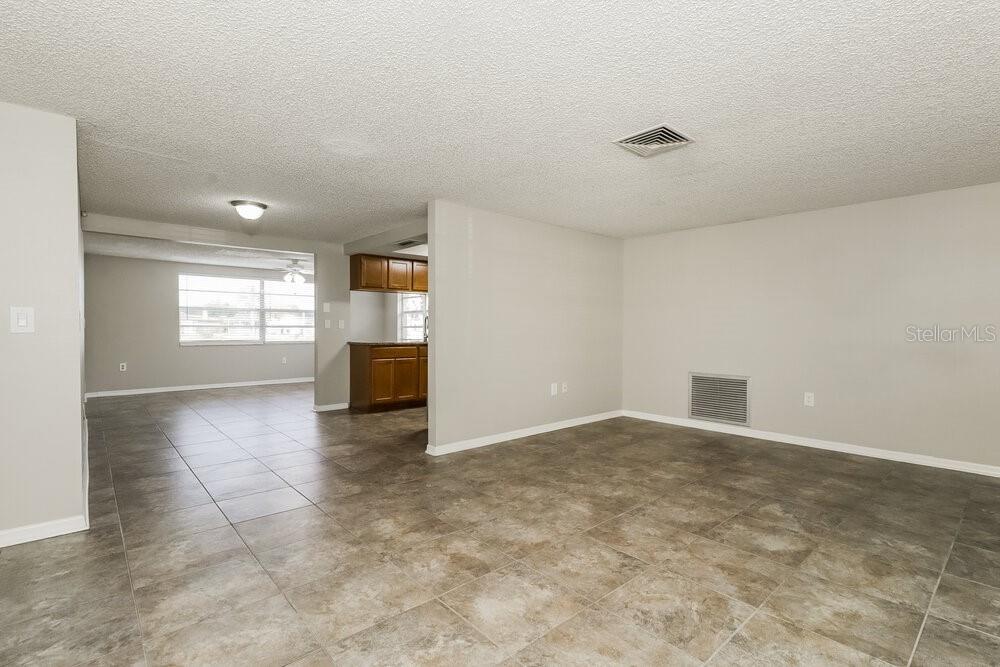 A living room with light gray walls and large tan floor tiles leads to a kitchen — 4347 OTTER WAY, NEW PORT RICHEY, FL