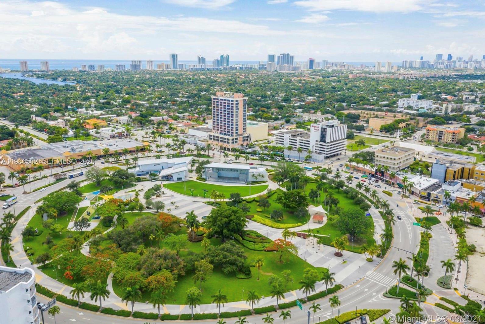 An aerial view of a city park featuring a central stage, green spaces, and surrounding buildings — 1830 Radius Dr # 522, Hollywood FL 33020, HOLLYWOOD, FL