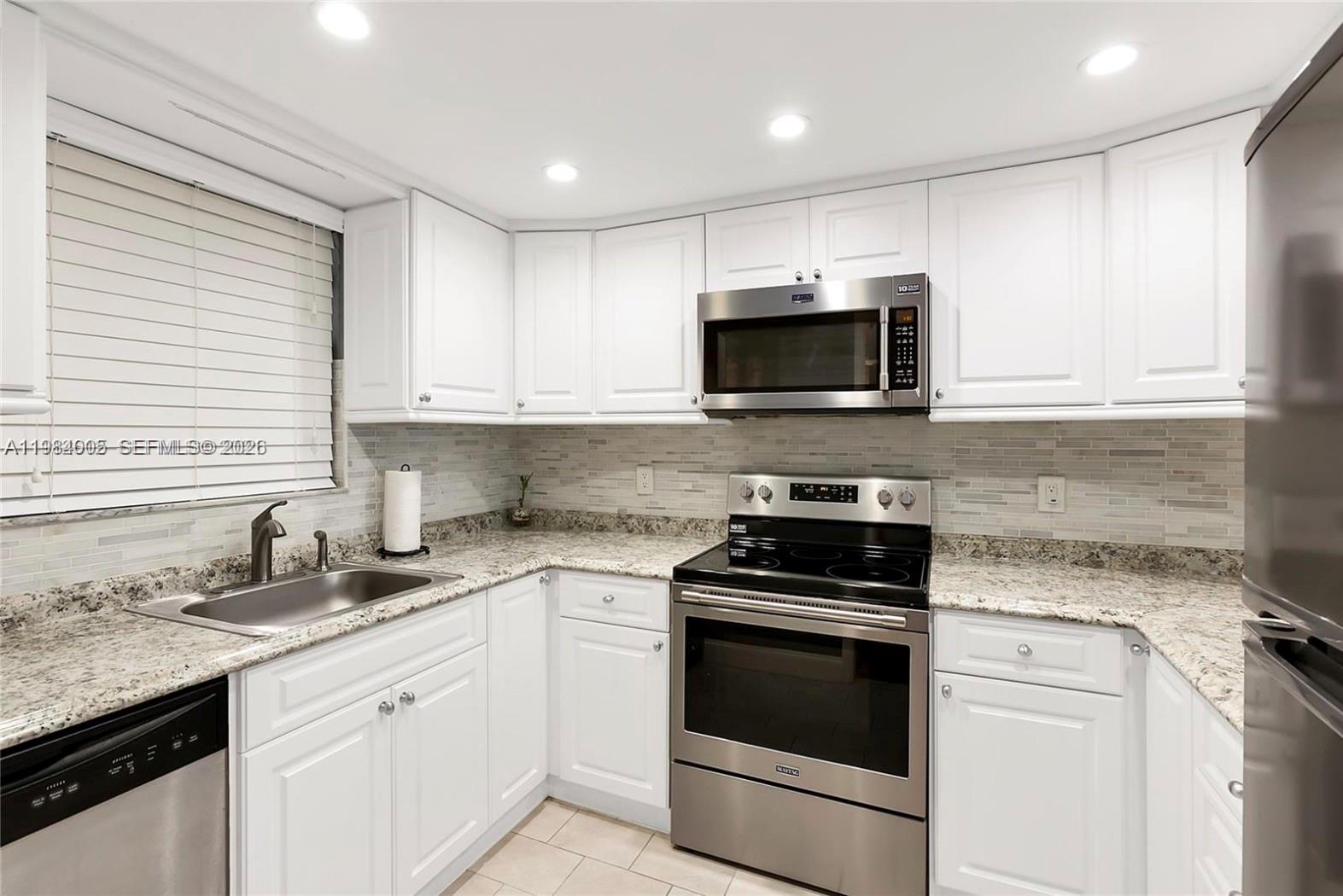 A kitchen features white cabinets, granite countertops, stainless steel appliances, and a tiled backsplash — 9430 Live Oak Pl # 407, Davie FL 33324, DAVIE, FL