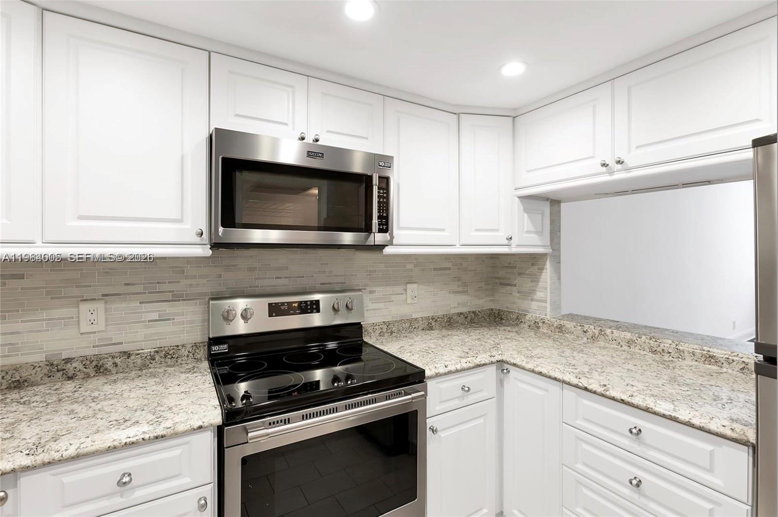 A kitchen features white cabinets, granite countertops, a tiled backsplash, and stainless steel appliances — 9430 Live Oak Pl # 407, Davie FL 33324, DAVIE, FL