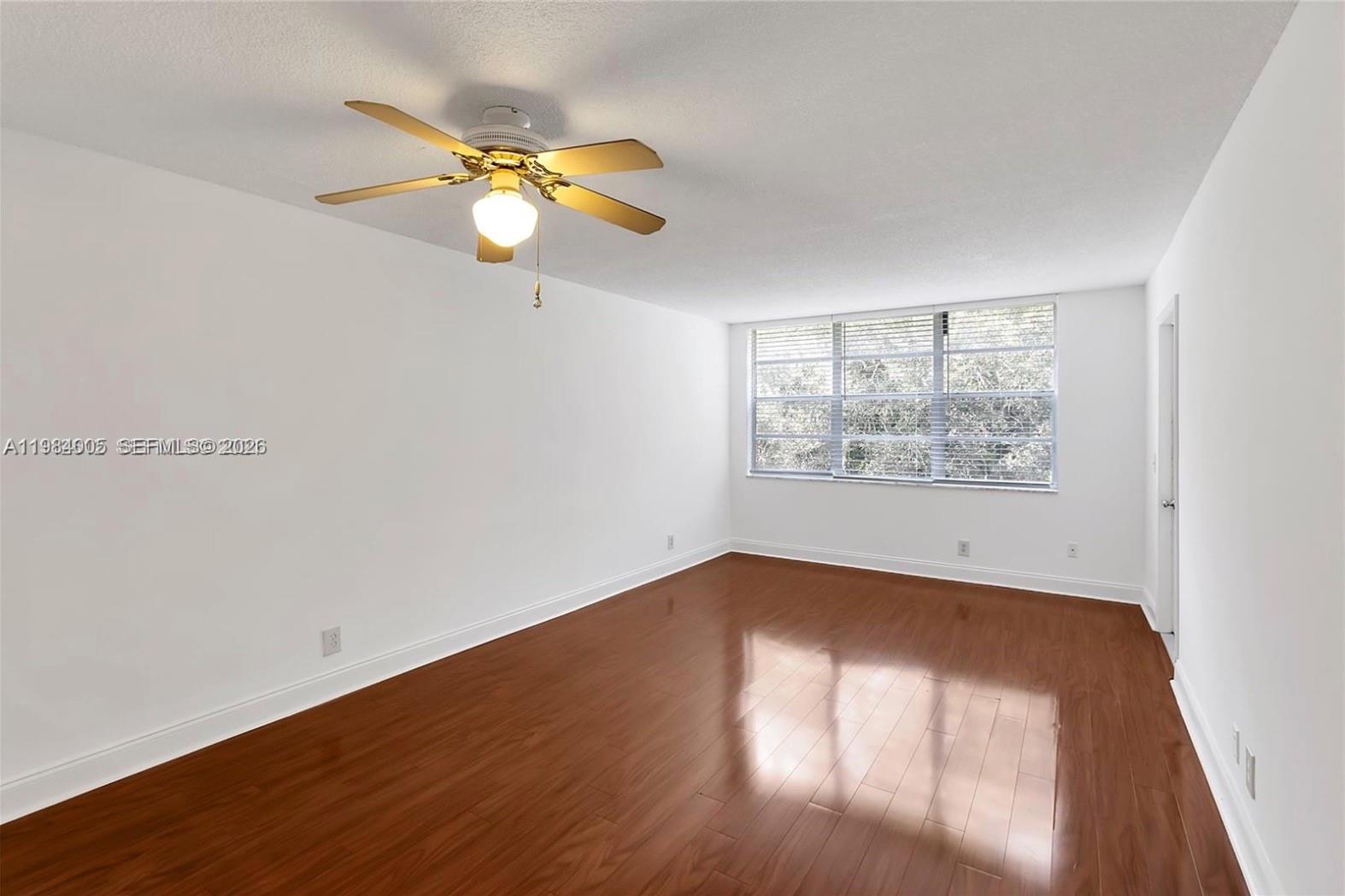 An empty bedroom features white walls, wood-look flooring, a ceiling fan, and a large window — 9430 Live Oak Pl # 407, Davie FL 33324, DAVIE, FL