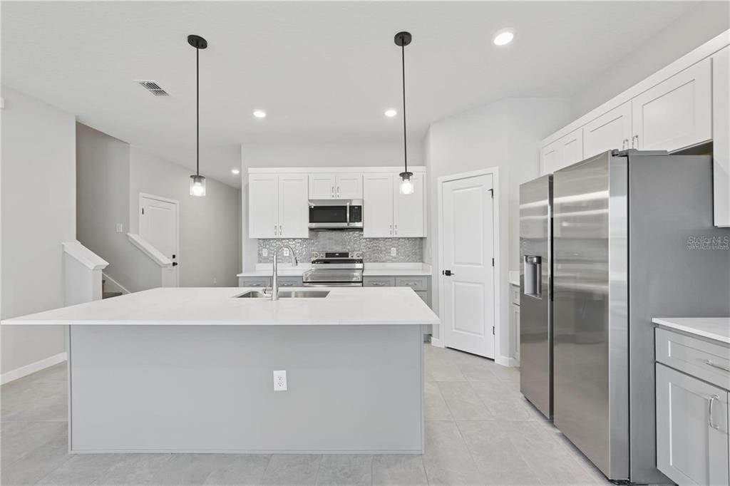 A modern kitchen features a large white island, stainless steel appliances, and white cabinetry — 84 SPRINGWOOD DRIVE, PALM COAST, FL