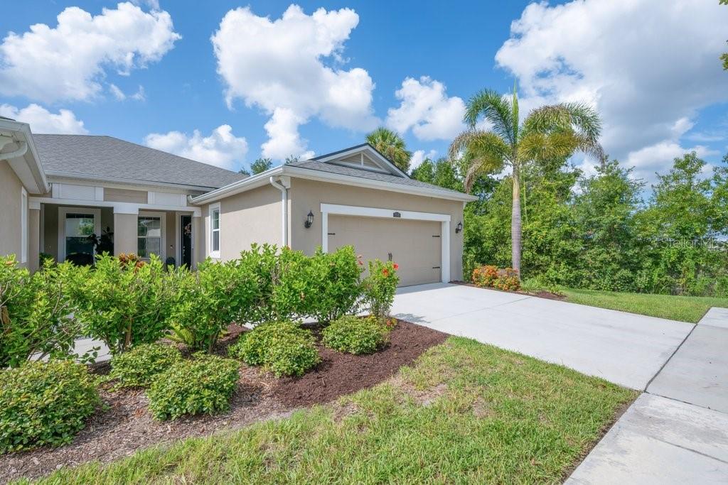 A beige single-story house features a two-car garage, a covered entryway, and landscaped front bushes — 11505 CAMBIUM CROWN DRIVE, RIVERVIEW, FL