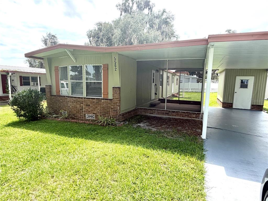 A single-story mobile home features a brick facade, a screened porch, and an attached carport — 5562 LANSING DRIVE, WILDWOOD, FL