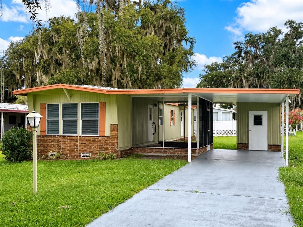 A single-story mobile home with a brick facade, screened porch, and attached carport — 5562 LANSING DRIVE, WILDWOOD, FL