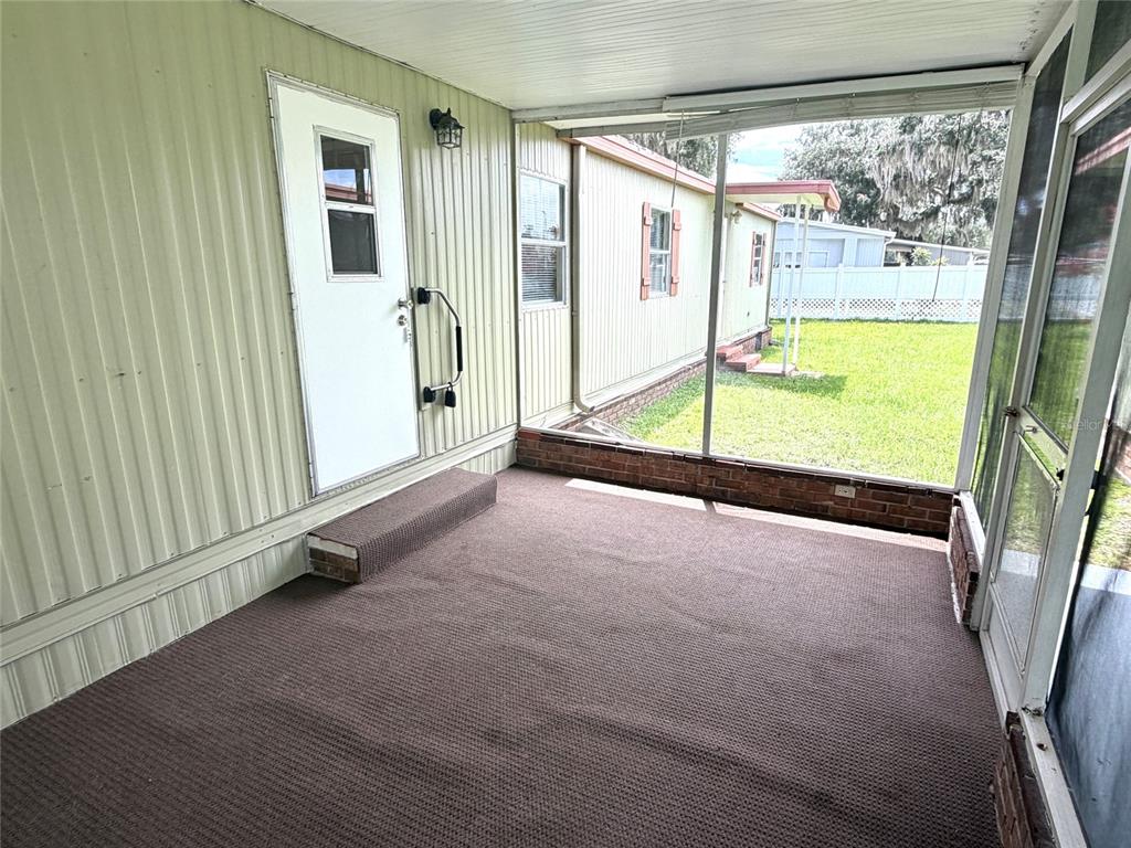 A carpeted, screened-in porch with a white door and a view of a grassy yard — 5562 LANSING DRIVE, WILDWOOD, FL
