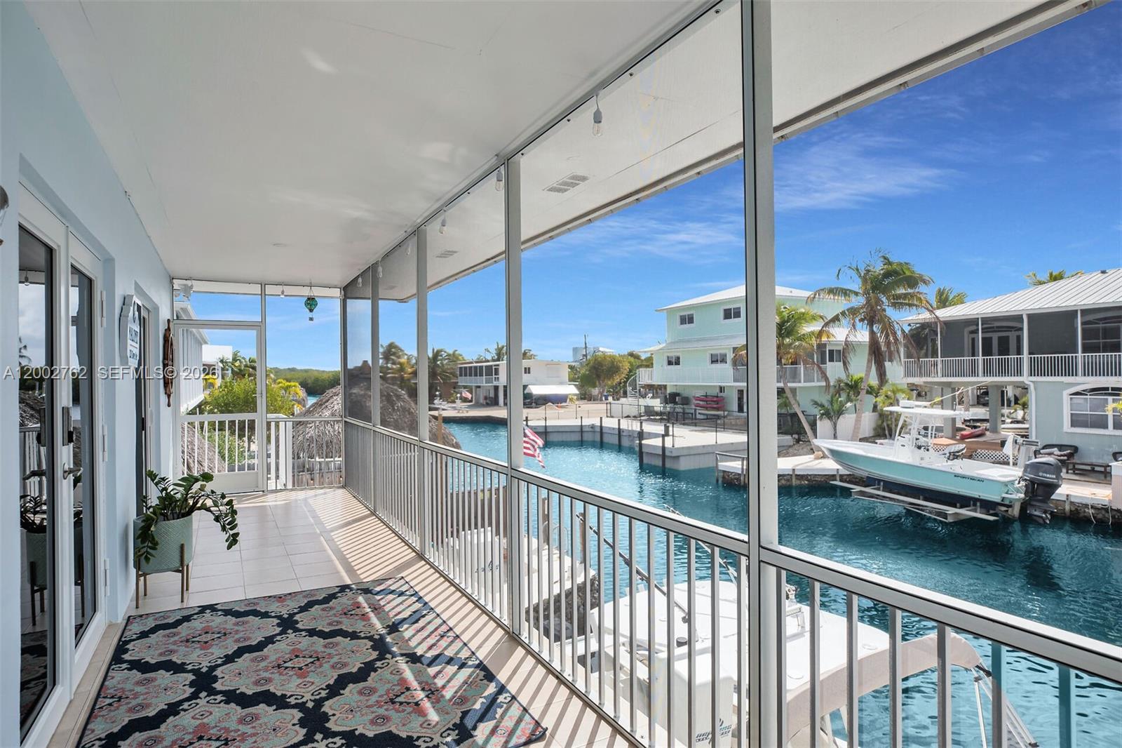 A screened-in balcony overlooks a canal with docked boats and nearby waterfront houses — 128 Dove Ave, Tavernier FL 33070, TAVERNIER, FL