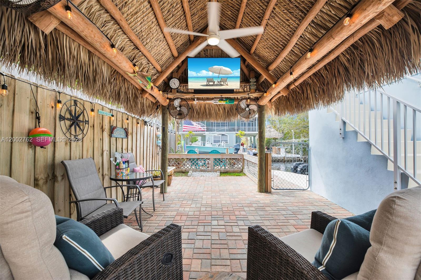 A covered outdoor patio features a thatched roof, brick flooring, and a mounted television — 128 Dove Ave, Tavernier FL 33070, TAVERNIER, FL