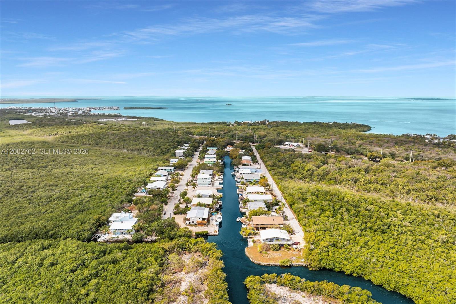 An aerial view shows a canal lined with houses surrounded by dense green vegetation — 128 Dove Ave, Tavernier FL 33070, TAVERNIER, FL