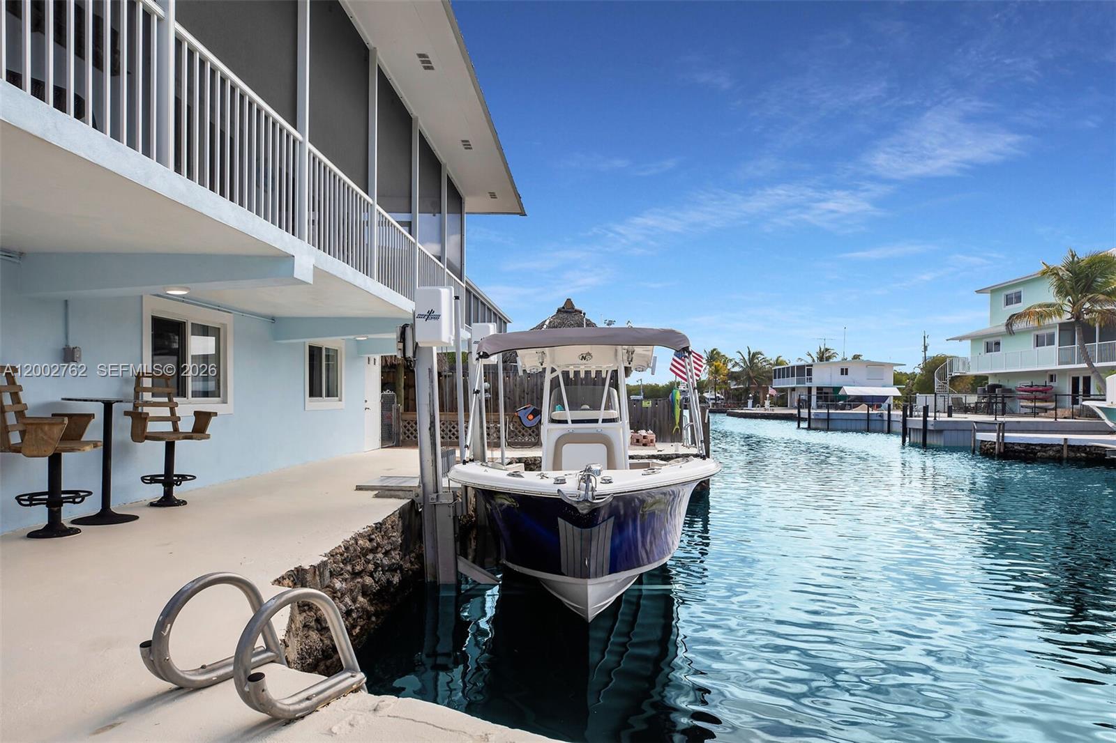 A boat is docked at a waterfront home with a covered patio and ladder — 128 Dove Ave, Tavernier FL 33070, TAVERNIER, FL