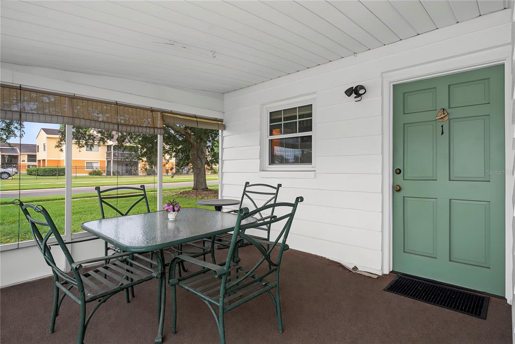 A covered patio features a glass-top dining table, four metal chairs, and a green door — 1001 PLANTATION DRIVE UNIT C1, KISSIMMEE, FL